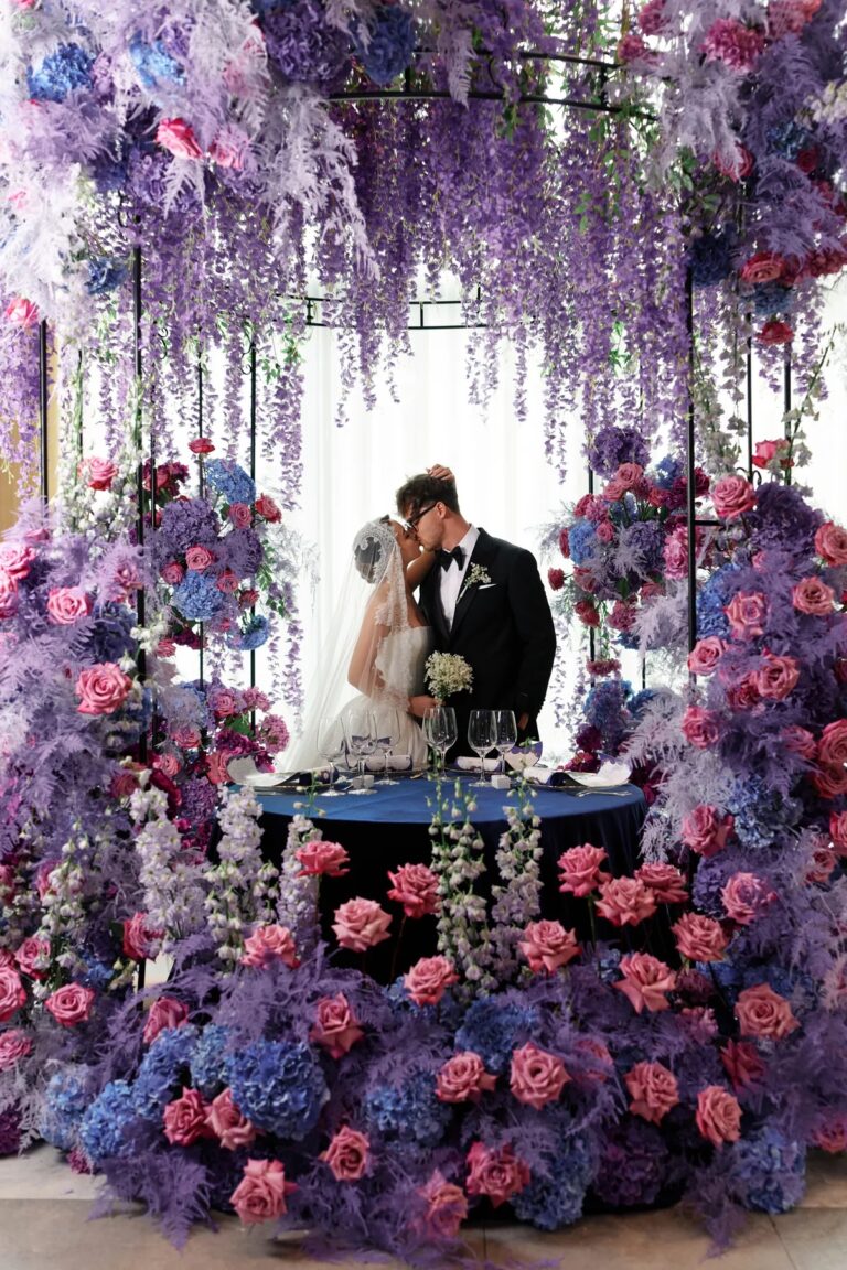 Couple at a sweetheart table surrounded by lilac and pink flowers, Geta Ungurean Agency