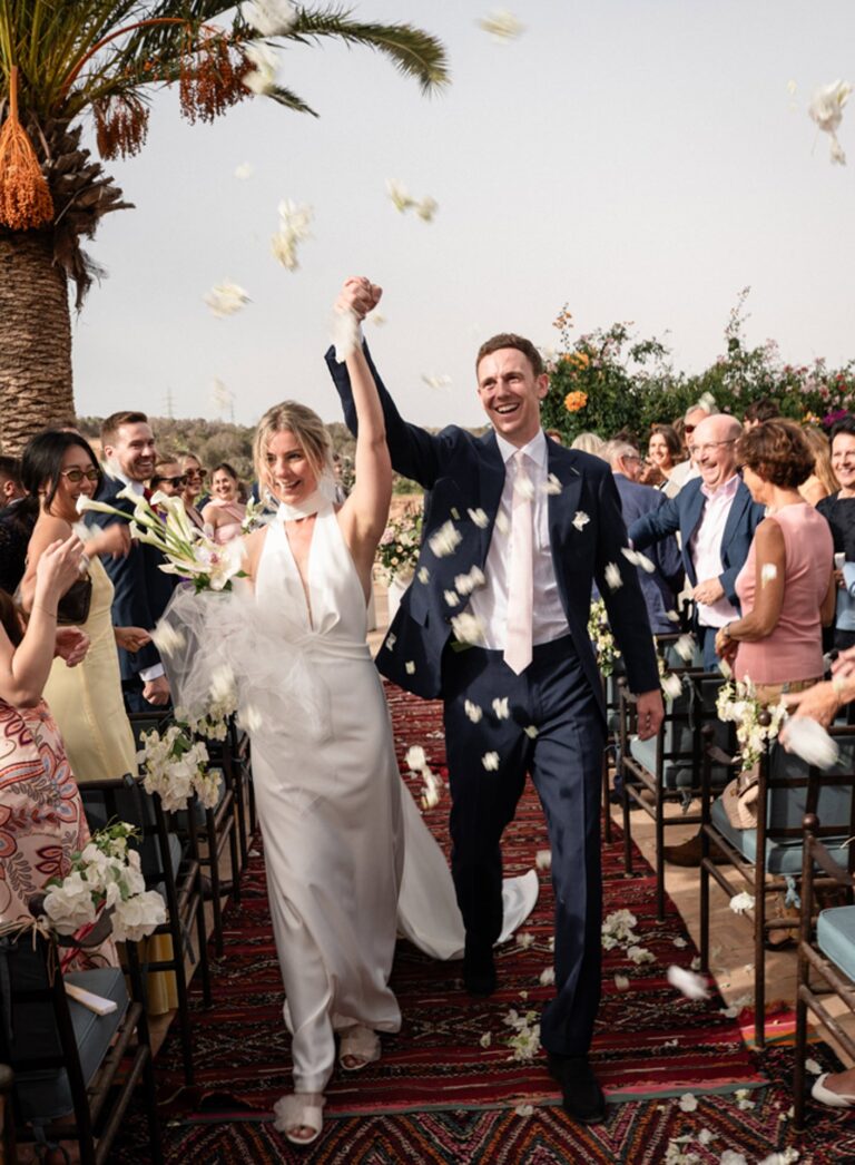 Bride and groom celebrating as petals fall along a rug-lined aisle beneath a palm, Giandomenico Cosentino Photography