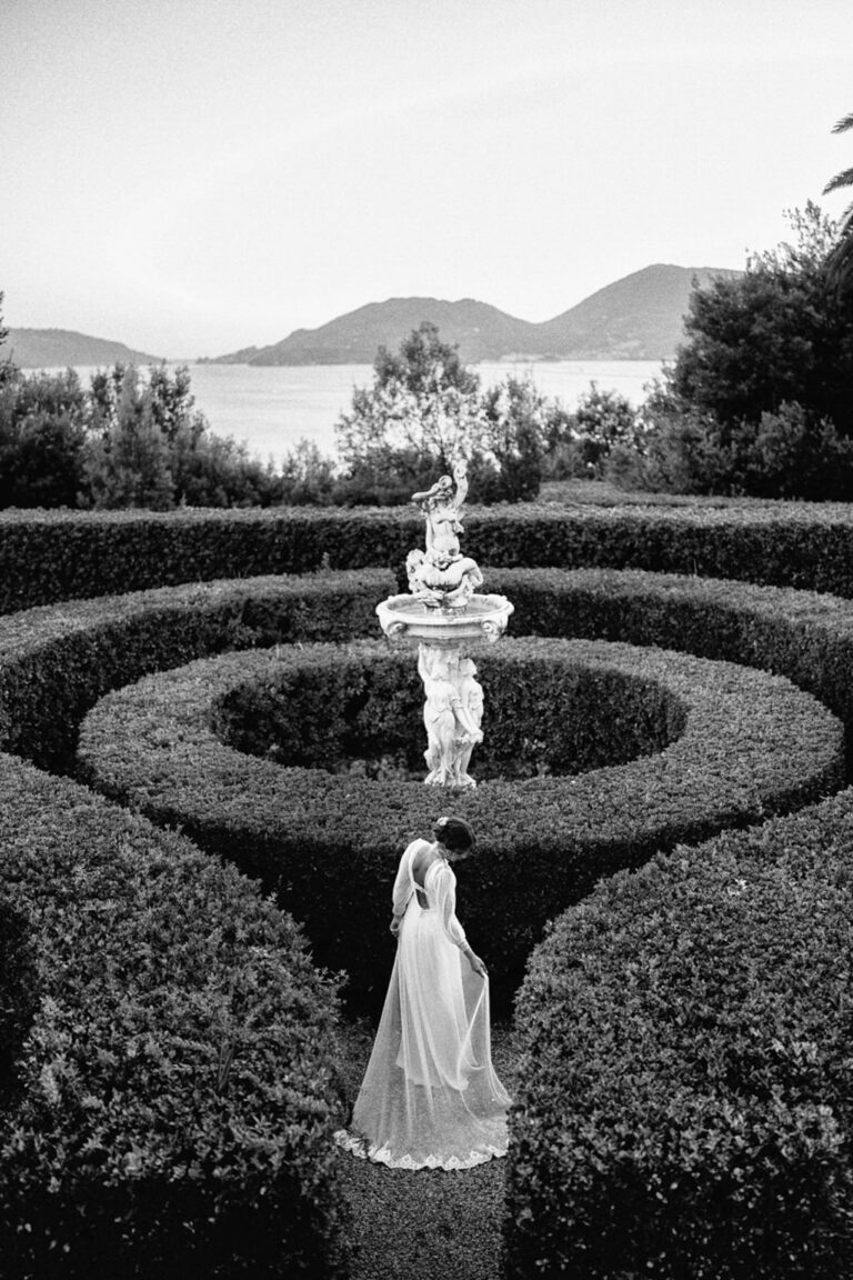A bride alone in a circular box-hedge garden above the water, in black and white, Giandomenico Cosentino Photography