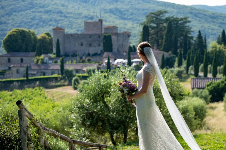 A bride with her bouquet looking across green hills to a hilltop castle, Giuliano Bausano