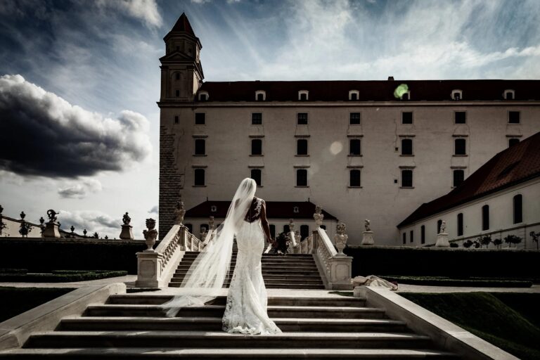 A bride climbing the stone stairs of a grand palace under a stormy sky, Giuliano Bausano
