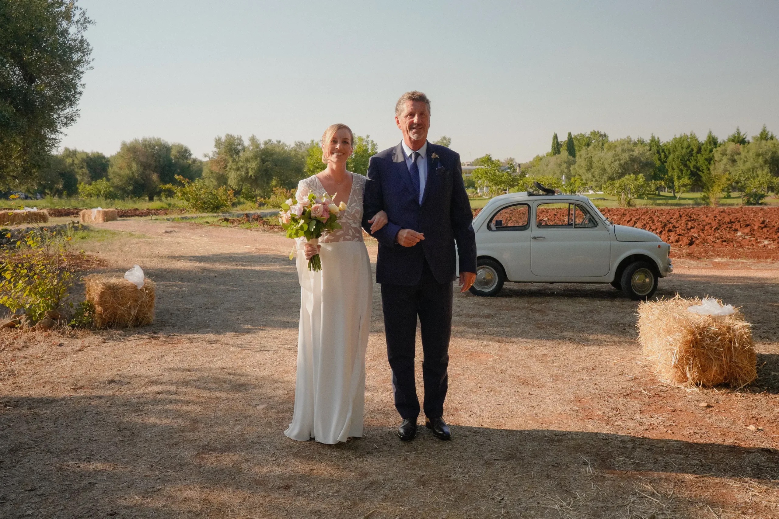 The bride walks to her ceremony along a country track, with a vintage Fiat 500 waiting, Puglia, Giuseppe Suma Weddings