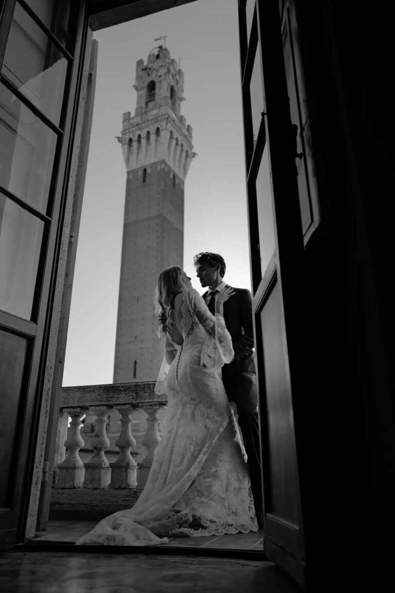 The couple framed in a balcony doorway with the Torre del Mangia beyond, Siena, Giuseppe Suma Weddings