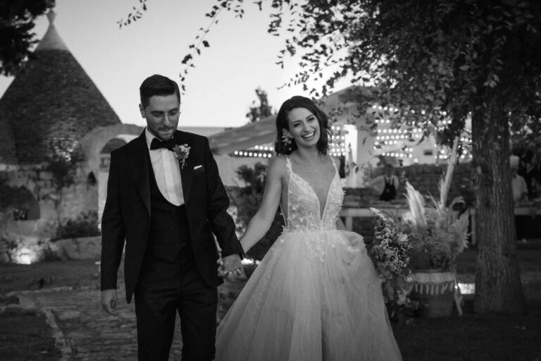 The couple walk through the evening party hand in hand, in black and white, Valle d'Itria, Puglia, Giuseppe Suma Weddings