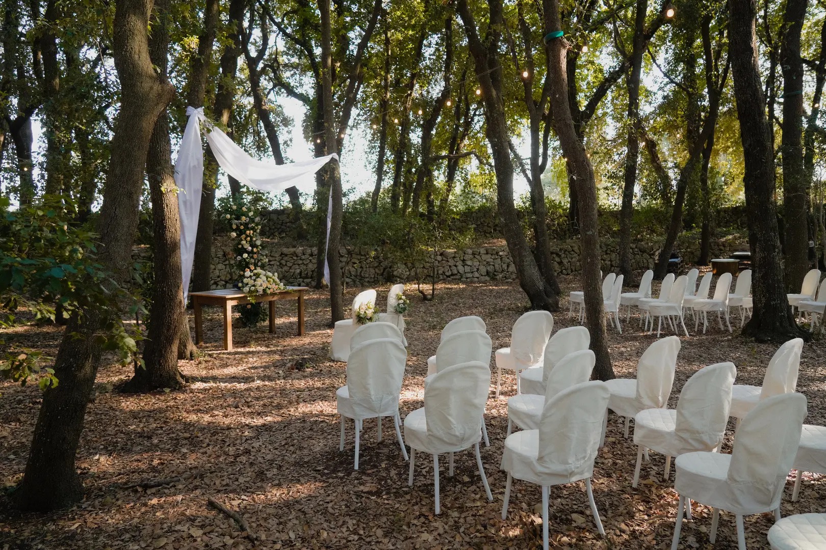 White chairs set for an outdoor ceremony beneath the trees, Puglia, Giuseppe Suma Weddings