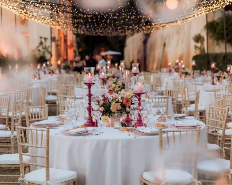 Round tables under strings of lights in a villa garden, fuchsia candlesticks and pastel flowers on white linen, Glam Events in Tuscany