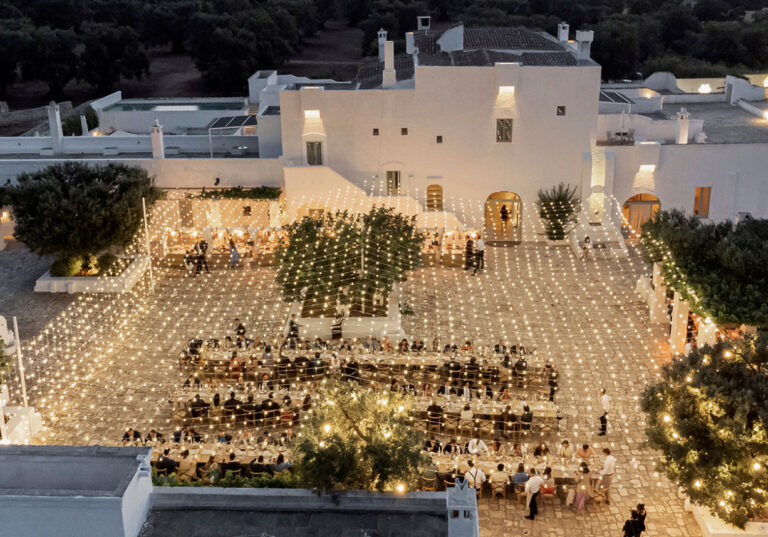 Dinner at dusk in the courtyard of a whitewashed masseria in Puglia, long tables under a canopy of lights, Glam Events in Tuscany