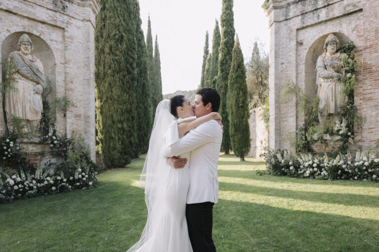 A couple in a cypress-lined garden between two stone figures in wall niches, white roses at their bases, Tuscany, Glam Events in Tuscany