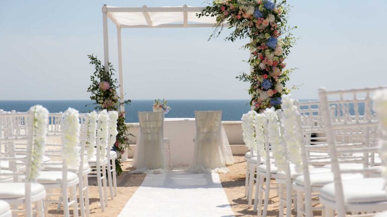 Seaside ceremony set-up: white chairs, floral arch and the Atlantic beyond, Glamour Algarve Weddings