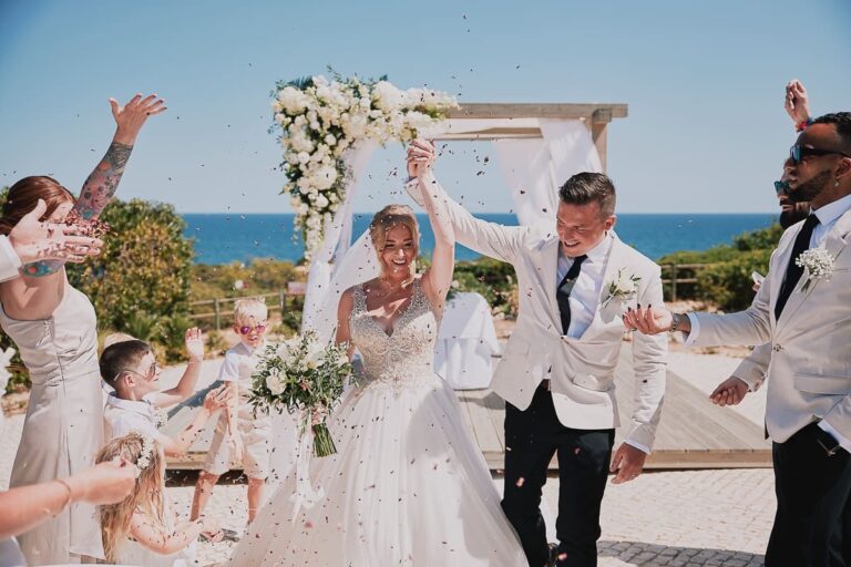 Couple leave the ceremony under a flower arch as guests cheer, Go2Wonderland