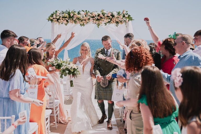 Guests throw confetti around the couple at a flower-topped arch, Go2Wonderland