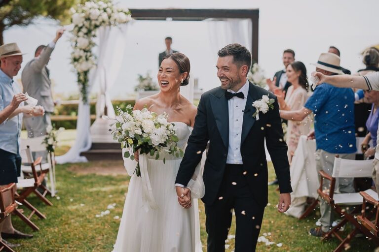 Couple walking back down the aisle past an arch of white flowers, Go2Wonderland
