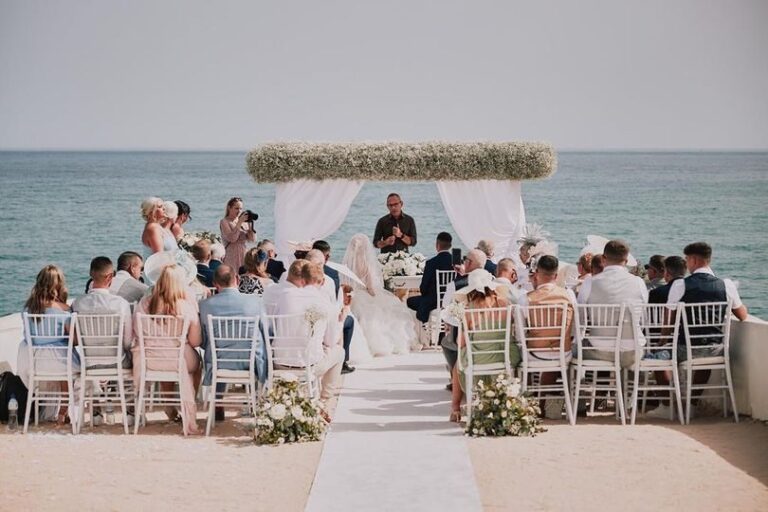 Seafront ceremony with guests seated before a floral arch, Go2Wonderland