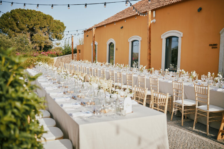 Long reception tables beneath festoon lights outside an ochre farmhouse, Go2Wonderland