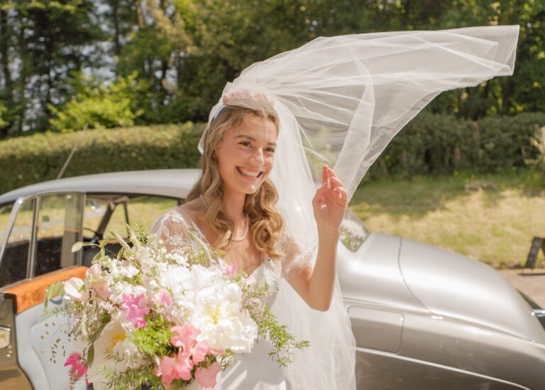 A bride's veil lifting in the breeze beside the wedding car, Gorgeous Films