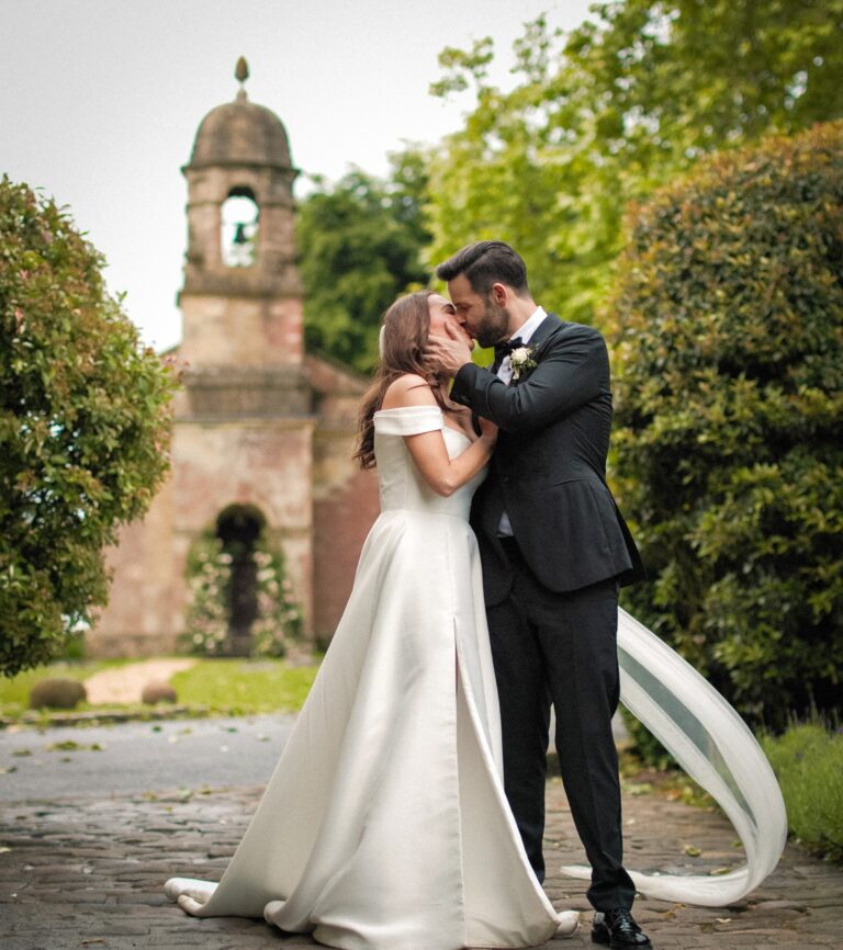 A kiss in front of a chapel bell tower, the bride's ribbon caught in the wind, Gorgeous Films