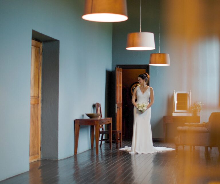 A bride waiting in a blue-walled room under low pendant lights, Gorgeous Films