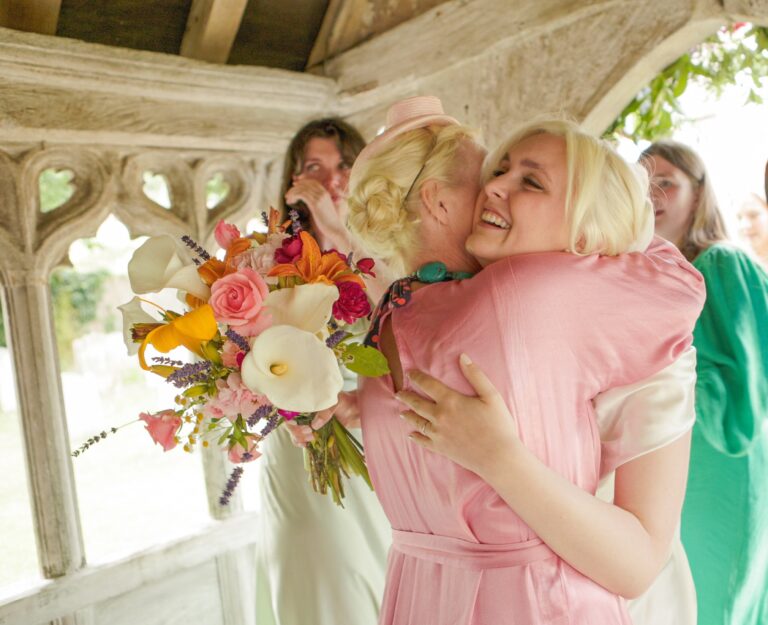 A bride embraced by a guest under a stone garden arch, Gorgeous Films