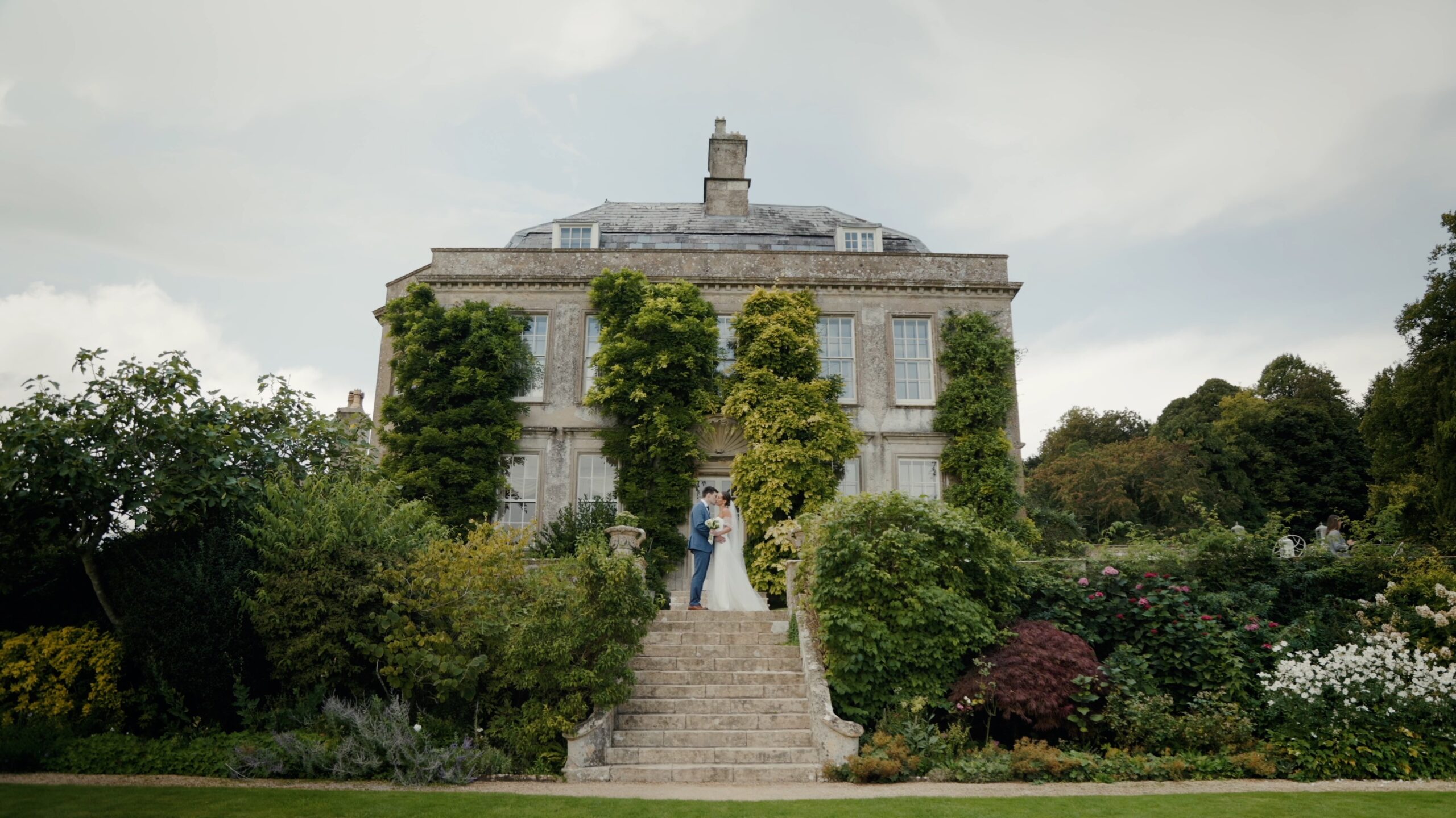 The couple on the stone steps of a wisteria-clad country house, framed by the garden, Gorgeous Films