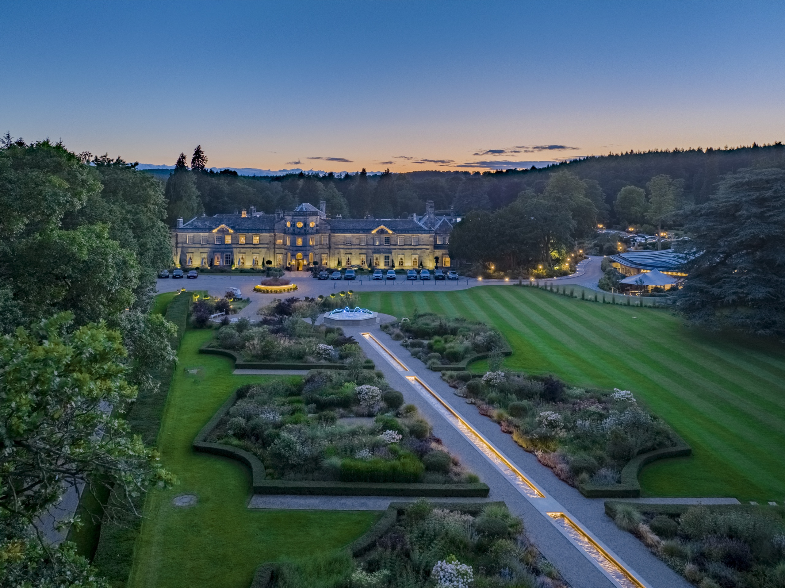 The formal garden and rill leading to the lit Hall at dusk, seen from above, Grantley Hall