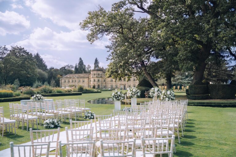White chairs set for an outdoor ceremony on the lawn, with old oaks and the Hall behind, Grantley Hall