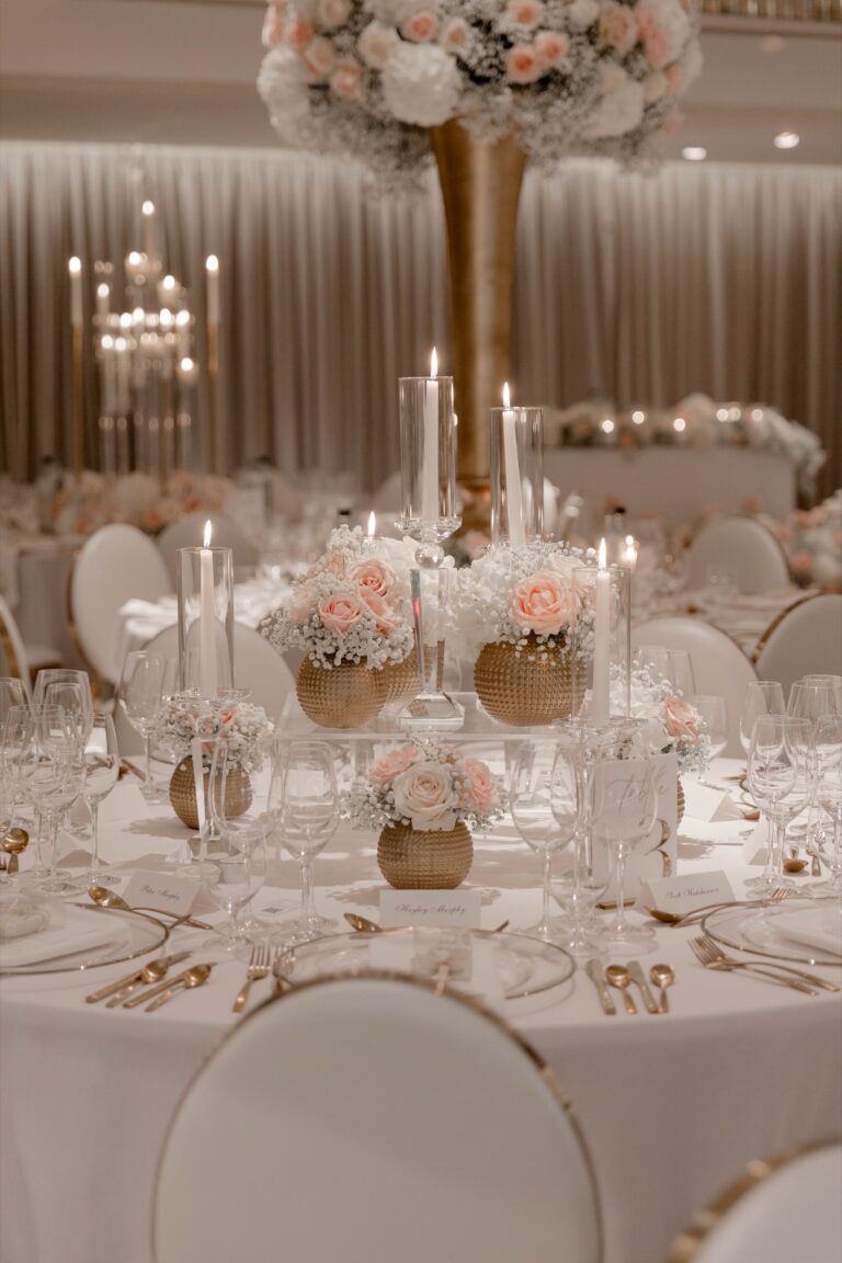 A candlelit round table with pink roses in gold vases and white chairs, Grantley Hall