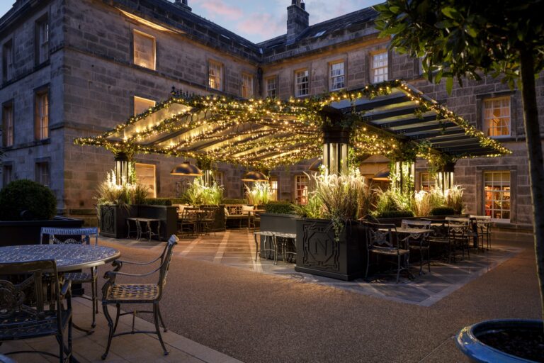 Norton Courtyard at dusk, with a lit pergola, planters and outdoor tables, Grantley Hall