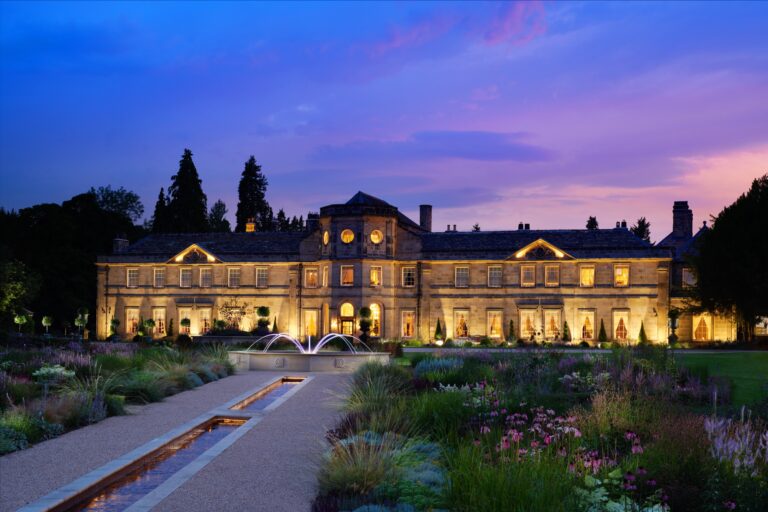 The south front of Grantley Hall lit at dusk, seen along the rill and fountain in the formal garden, Grantley Hall