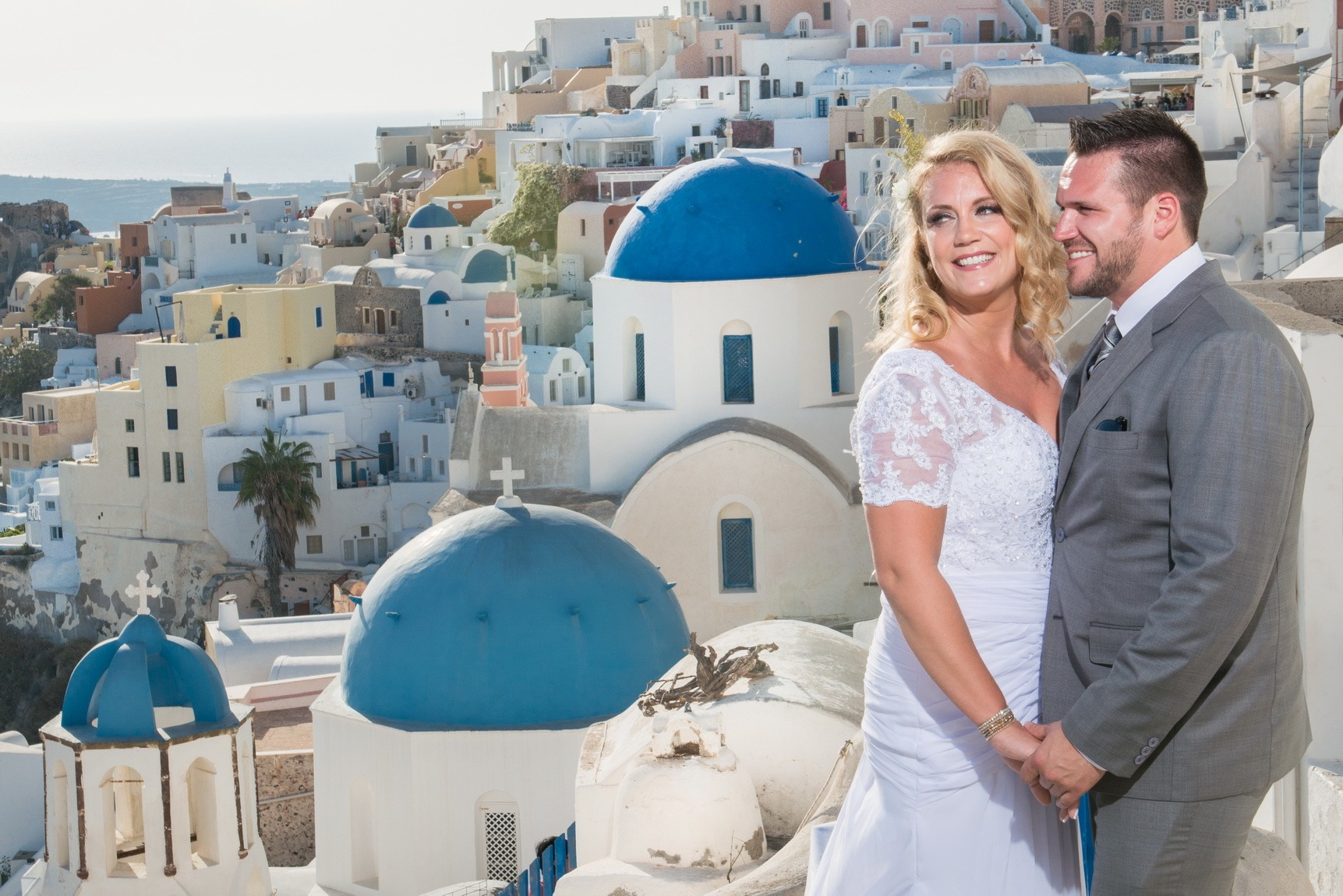 Couple posing beside the blue domed churches of a Santorini village, Greek Dream Planners
