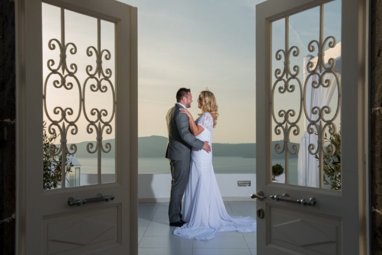Couple embracing between open wrought iron doors above the sea, Greek Dream Planners