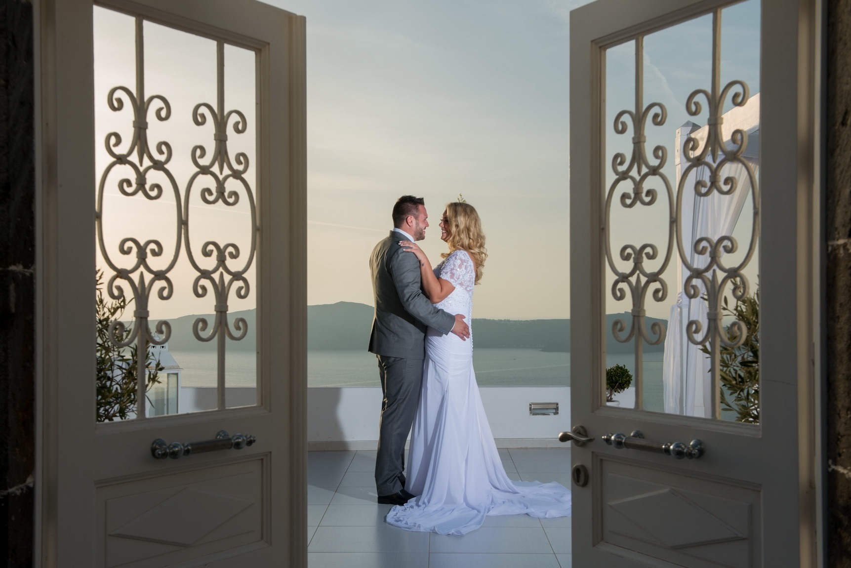 Couple embracing between open wrought iron doors above the sea, Greek Dream Planners