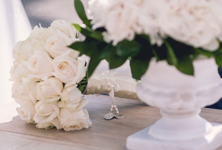 Bouquet of white roses with a charm on a wooden table, Greek Dream Planners