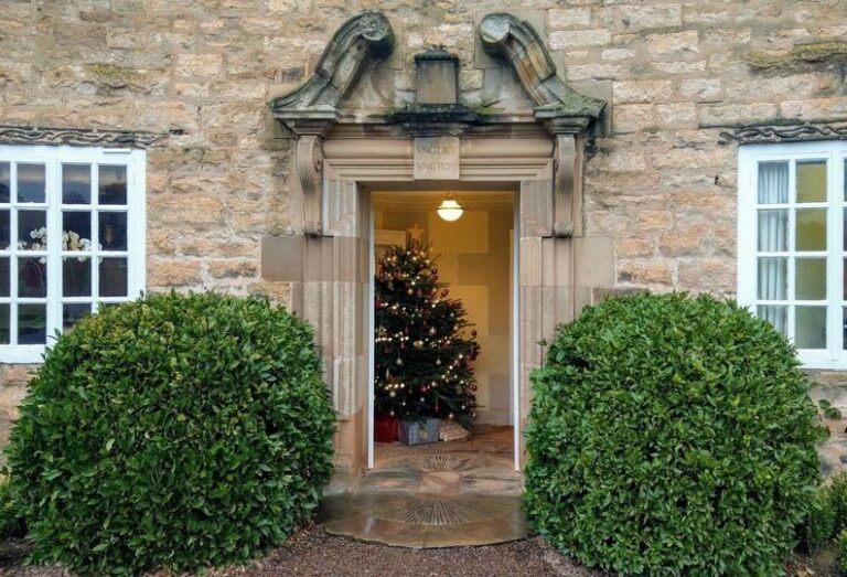 A carved Lutyens stone doorway framed by clipped topiary, a glimpse of the hall within, Greywalls Hotel & Chez Roux