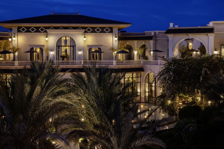 The palace facade lit at night among palms, Hôtel Palais Ronsard Relais & Châteaux