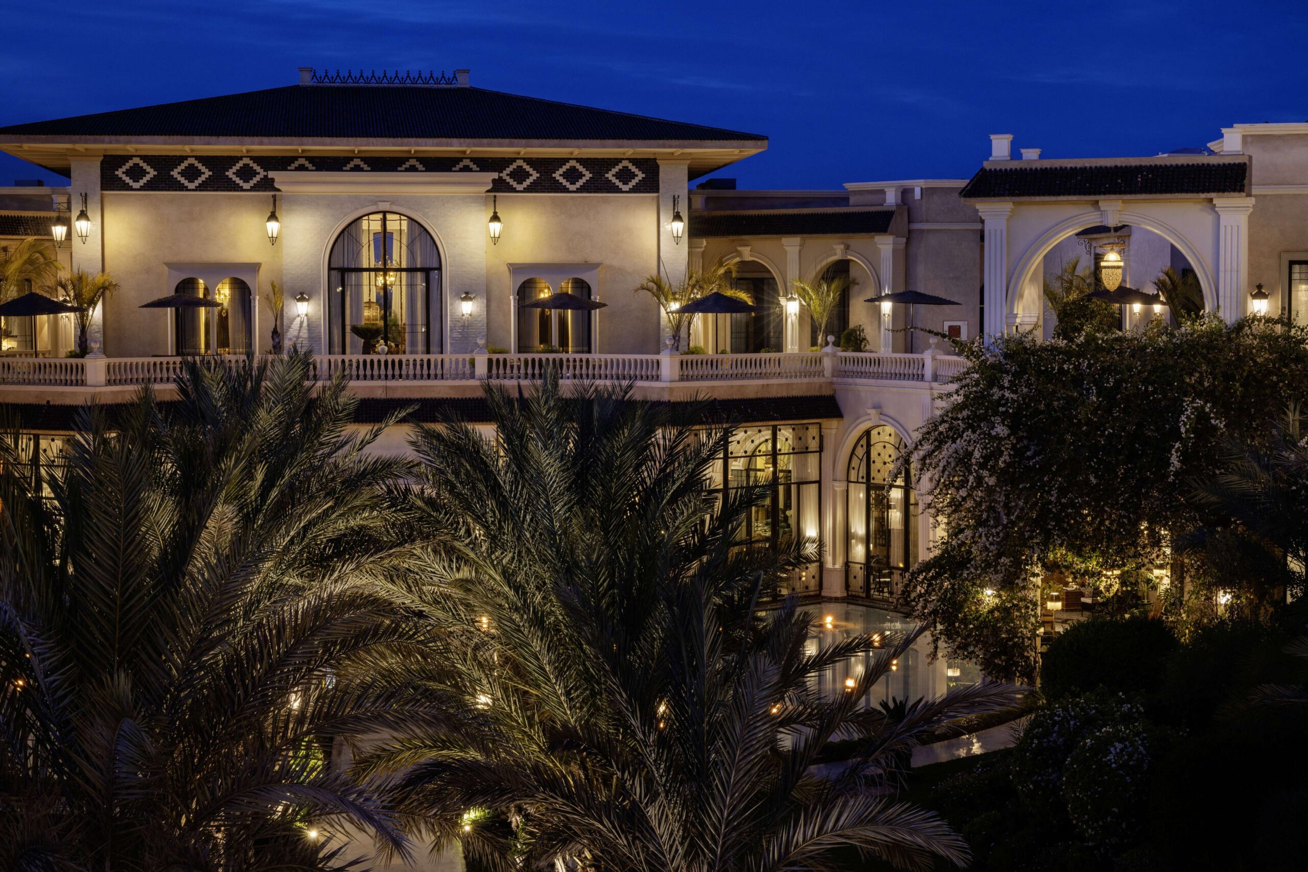 The palace facade lit at night among palms, Hôtel Palais Ronsard Relais & Châteaux