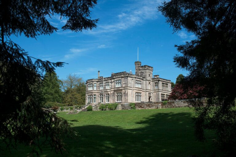 The manor house beneath a wide sky, its gables and turrets above sweeping estate lawns, Hampton Manor