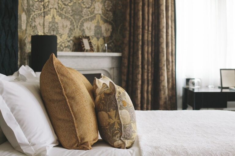 A bedroom detail, gold cushions on a white bed beside a fireplace, Hampton Manor