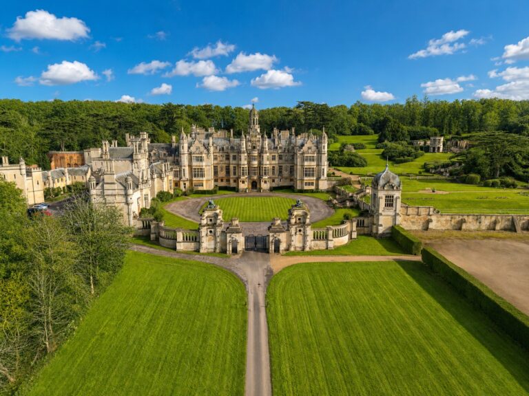Aerial view of the entrance front, the oval forecourt lawn and the gatehouse, with the straight drive running out between mown lawns, Harlaxton Manor