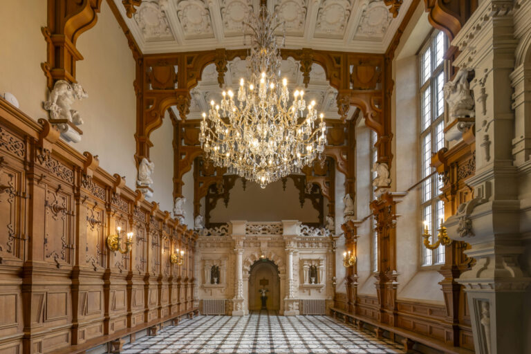 The Great Hall with oak panelling, a carved timber roof, crystal chandelier and the stone screen at the far end, Harlaxton Manor