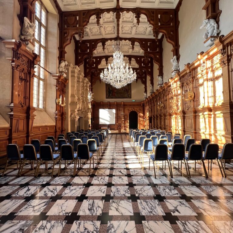 Rows of chairs set on the marble floor of the Great Hall, lit by tall windows, Harlaxton Manor