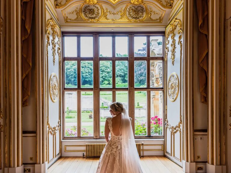 A bride seen from behind at the tall window of the Gold Room, looking out over the gardens, Harlaxton Manor