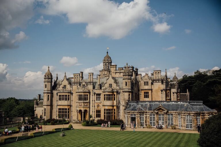 The garden front and the long glass conservatory above a striped lawn, with wedding guests gathering on the terrace, Harlaxton Manor