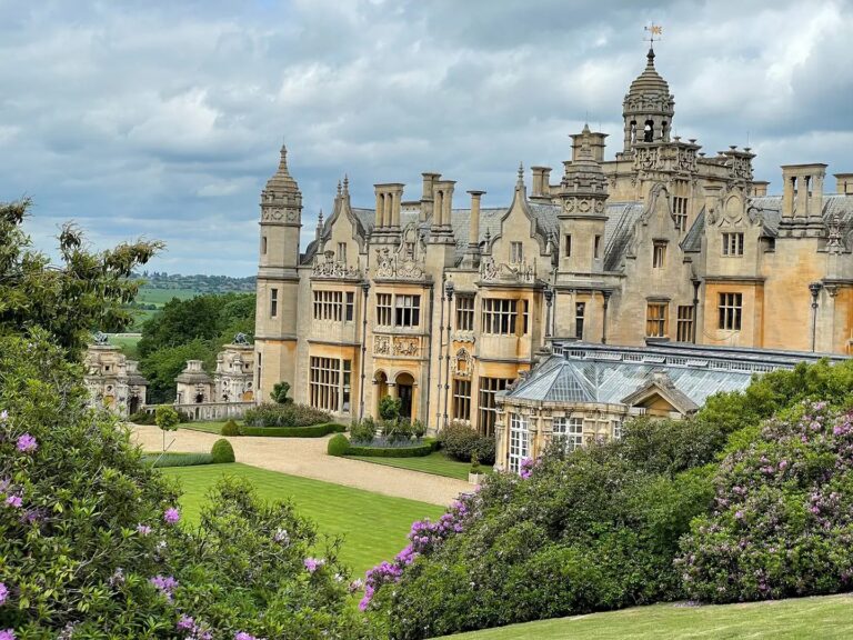 The manor and conservatory above banks of flowering rhododendrons, with the Vale of Belvoir beyond, Harlaxton Manor