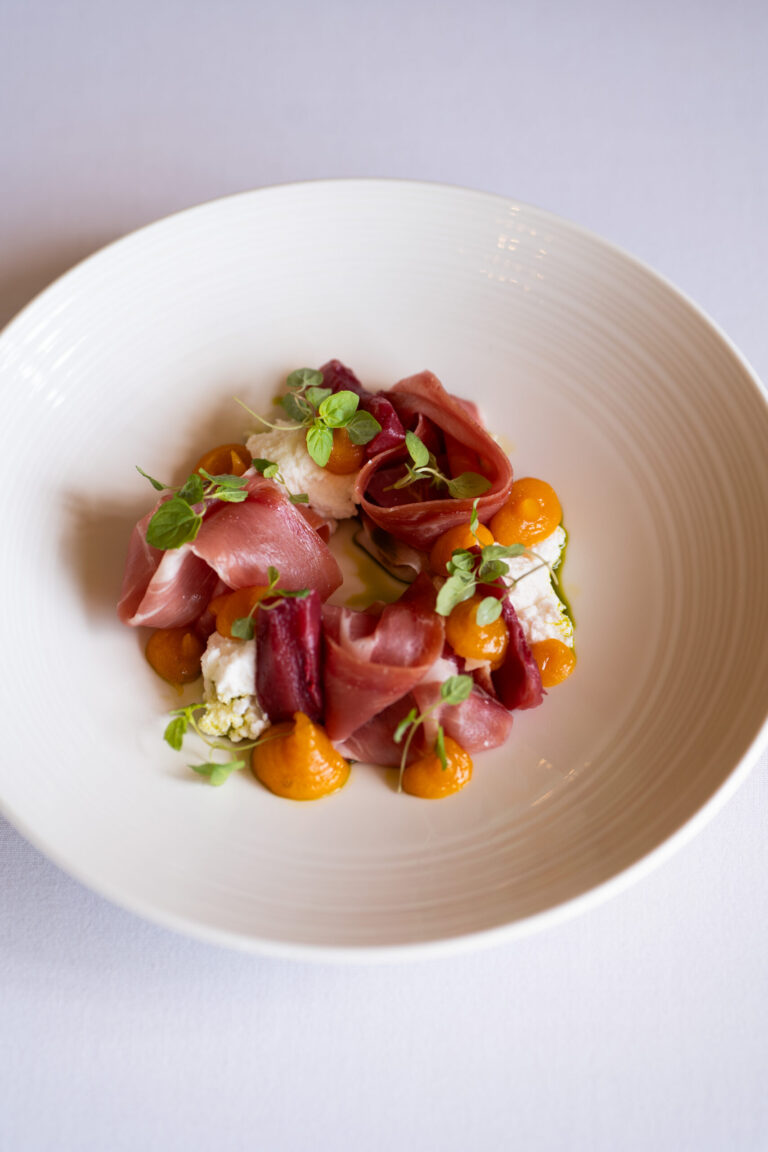 A plated starter of cured ham, burrata and apricot on a white bowl, Harlaxton Manor