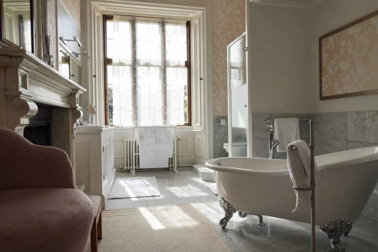 A bathroom inside the manor with a roll-top bath, marble surround and a tall sash window, Harlaxton Manor