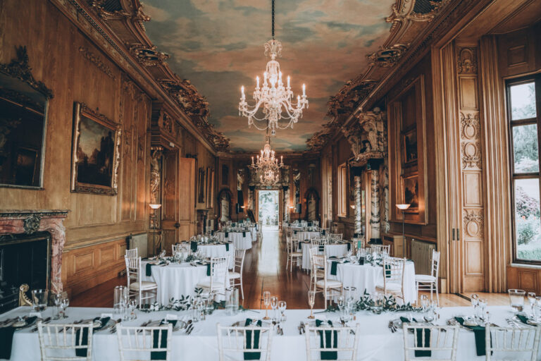 Long tables with white linen and green napkins running the length of the Long Gallery, with chandeliers above, Harlaxton Manor