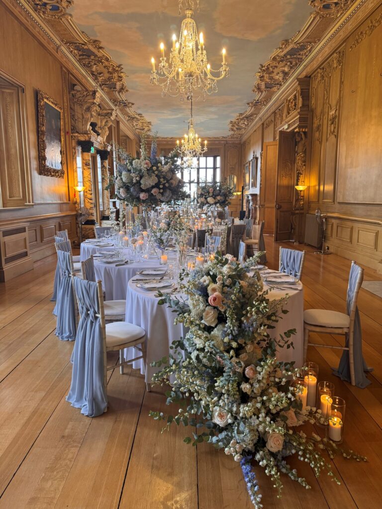 Round tables in the Long Gallery dressed with pale blue linen, candles and a cascading floral arrangement, Harlaxton Manor