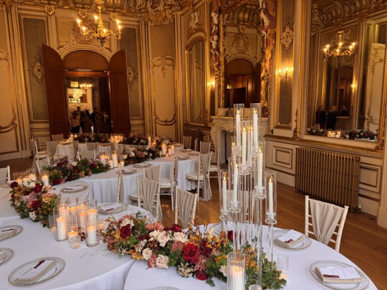 Round tables with candelabra and red and orange flowers in a gilded state room with mirrored walls, Harlaxton Manor