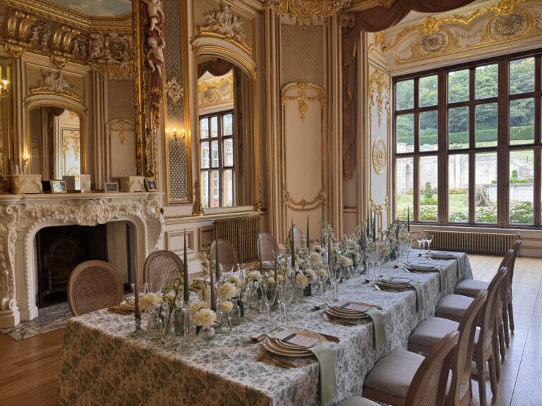 A single long table with floral linen and greenery for a small wedding, in a white and gold room overlooking the gardens, Harlaxton Manor