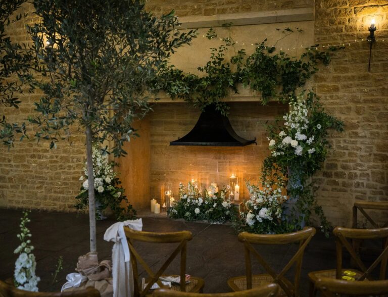 A ceremony beneath a floral arch by the barn fireplace, Haselbury Mill